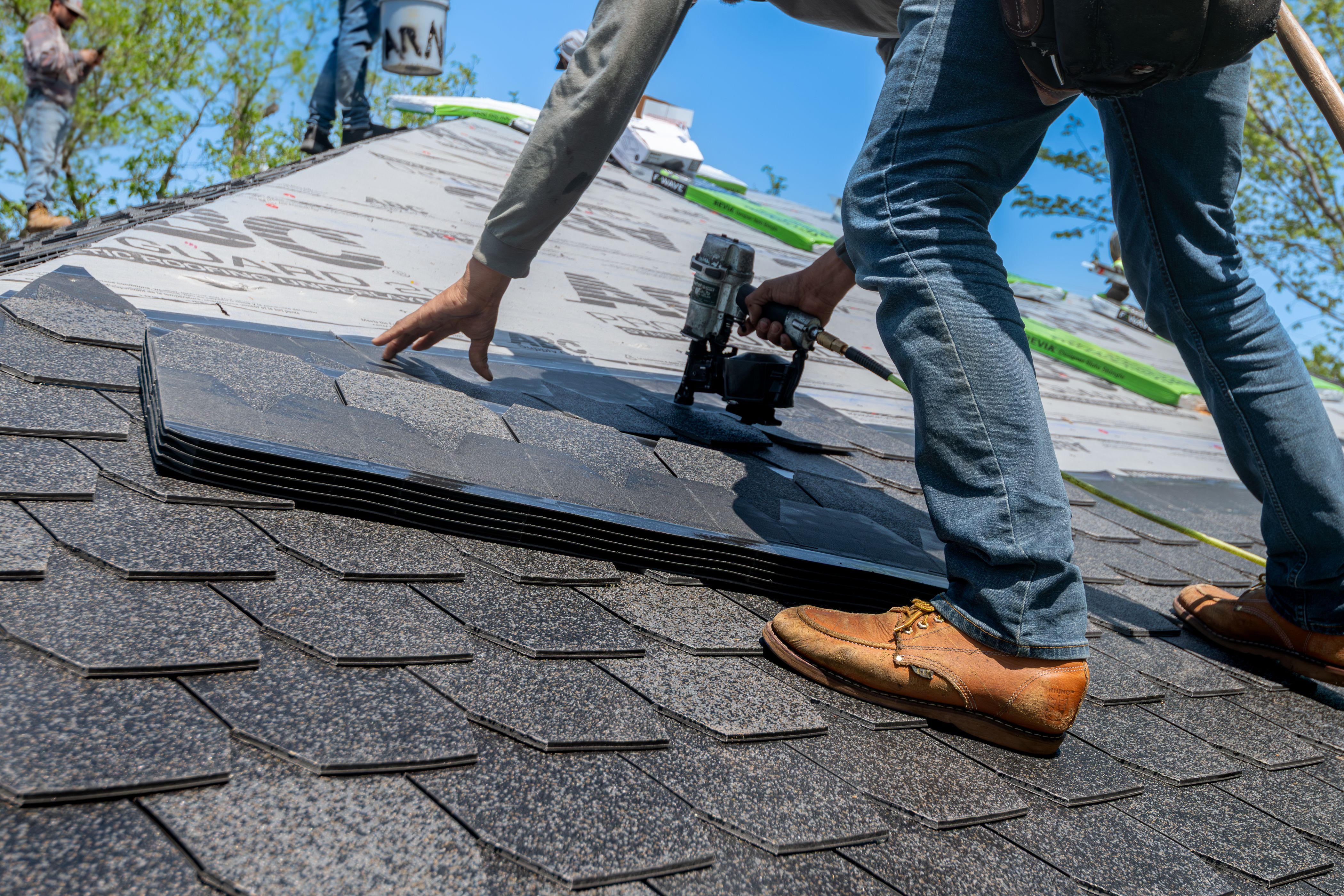Roofer installing shingles with a nail gun on a residential job